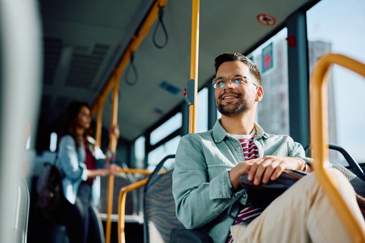 Man zit tevreden in de bus met tas op schoot. Reiziger is gefotografeerd vanaf onder.